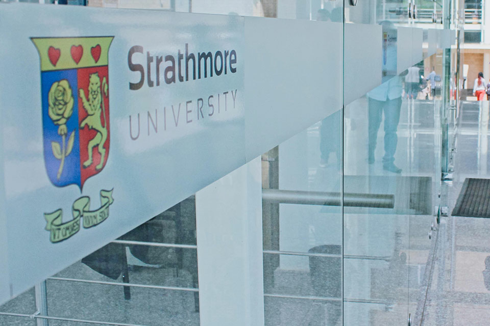 Strathmore University logo is shown on glass doors reflecting students who are walking to class.